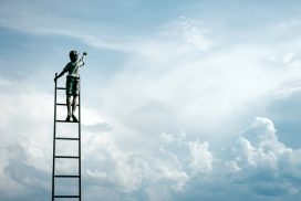 Un niño subido en una escalera pinta nubes en el cielo, coaching para conseguir objetivos realistas apuntando alto 