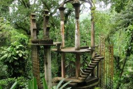 Una edificación de madera, con columnas y distintos niveles entremezclada con y en un bosque. 