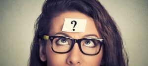 Una mujer dirige su mirada hacia un post it en su frente con un interrogante. 
