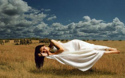 Una mujer joven, vestida de blanco, duerme, y levita sobre un campo. En terapia transpersonal trabajamos con los sueños. 