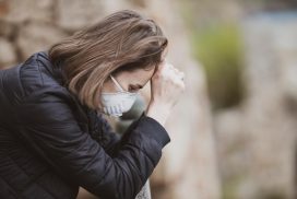 Una mujer con mascarilla sostiene su cabeza desde la frente con la mano derecha, parece estresada. 