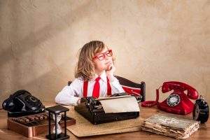 Una niña ante una máquina de escribir antigua y rostro pensativo. Parece estar buscando inspiración