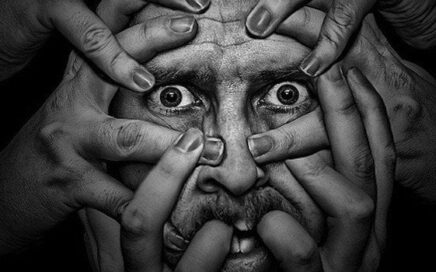 Rostro de un hombre, asustado,  agarrado por varias manos; metáfora de tácticas de manipulación psicológica.
