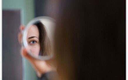 En un espejo se ve muy parcialmente el rostro de una mujer, metáfora de la invisibilización de la participación femenina. 