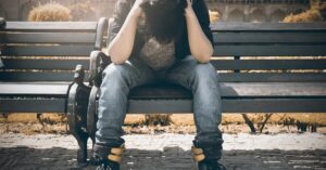 Un hombre joven sentado abatido en un banco en la calle. Las  masculinidades críticas contemplan la herida emocional que el patriarcado inflige al hombre. 