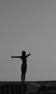 Sobre un fondo oscuro, la silueta de una mujer con los brazos abiertos en gesto expansivo. 